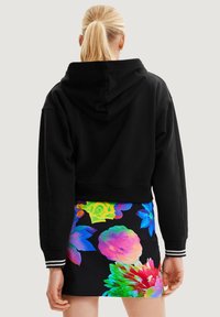 Czarna krótka bluza z kapturem i sznurkiem do ściągania. Połączona z kolorową spódnicą w kwiatowy wzór z jasnymi kolorami na ciemnym tle.