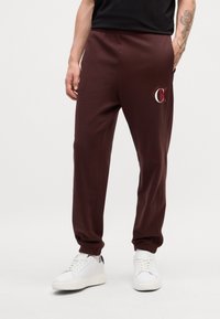 Karmaša bikses ar elastīgu jostasvietu, sānu kabatām un baltu logo uz augšstilba. Apvienotas ar baltām sporta apaviem. Gluda tekstūra.