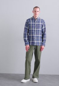 Πουκάμισο με καρό σχέδιο σε μπλε και πράσινο, συνδυασμένο με ελαιόχρωμο παντελόνι και λευκά sneakers. Λείο ύφασμα με άνετη εφαρμογή.