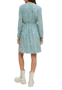 Abito a maniche lunghe realizzato in tessuto leggero con un motivo astratto blu e verde, vita cintrata e gonna svasata, abbinato a stivaletti bianchi alla caviglia.
