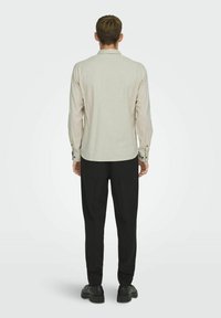 Camisa de manga larga gris claro con dobladillo recto, puños con botones y una textura sutil, combinada con pantalones negros y zapatos negros.