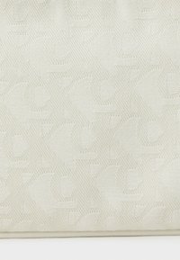 Borsa a tracolla color crema con texture, caratterizzata da un design a motivo con dettagli del logo sottili. Realizzata in tessuto resistente con una finitura liscia.