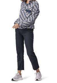 Fleece-pull i vitt och marinblå geometrisk mönster med knäppt krage och marinblå ficka; parat med mörka tajta byxor och ljusa sneakers.