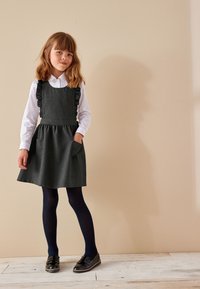 Hallidega hall kleit koos volangidega rihmadega, volditud vöökoha ja taskutega. Kombineeritud valge särgiga, mereväe siniste sukkpükste ja mustade kingadega puidust põrandal.