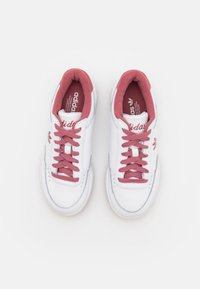 Baltieji ādas sporta apavi ar rozā akcentiem, ar plakaniem rozā shoelaces, izšūtu zīmolu un klasisku zemu dizainu.