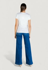 Camiseta blanca de manga corta combinada con vaqueros de pierna ancha en azul. El conjunto se completa con tacones beige, mostrando un estilo casual.