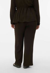 Haut péplum marron texturé à manches longues, associé à un pantalon fluide foncé et des ballerines à motifs. Accent sur la simplicité et le confort.