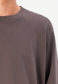 Tricou gri din bumbac, cu guler rotund, cu o textură moale, având un guler ribant și o croială lejeră. Fără logo-uri sau modele vizibile.