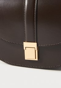 Borsa a mano in pelle marrone scuro con un clasp rettangolare dorato e cuciture a contrasto lungo le cuciture. Forma arrotondata con texture liscia.