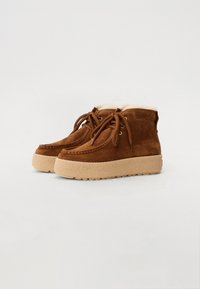 Bottes de cheville en daim marron avec une doublure en fourrure douce, bout rond, semelle en caoutchouc beige épaisse et lacets marron avec œillets en métal.