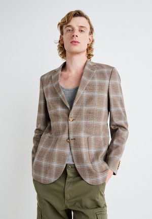 Brauner Kariertes Blazer aus strukturiertem Stoff, mit Reverskragen, zwei Knöpfen und schlanker Passform, kombiniert mit einem grauen Oberteil und olivgrünen Hosen.