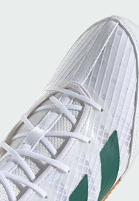 Scarpa atletica bianca con tomaia testurizzata e dettagli verde, lacci piatti e pannello laterale liscio e lucido. Suola in gomma visibile.