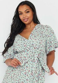 Abito a portafoglio floreale in un delicato verde menta, con maniche corte, vita legata e un motivo delicato di piccoli fiori rossi e blu.