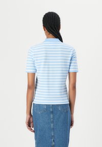 Blå og hvid stribet polo skjorte med korte ærmer, der har en klassisk krave og en tætsiddende pasform. Bæres med en denim nederdel.