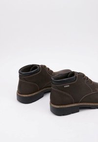 Par de botas de cuero marrón oscuro hasta el tobillo con cuellos acolchados negros y suelas de goma gruesa, mostradas de perfil y por detrás sobre un fondo blanco.