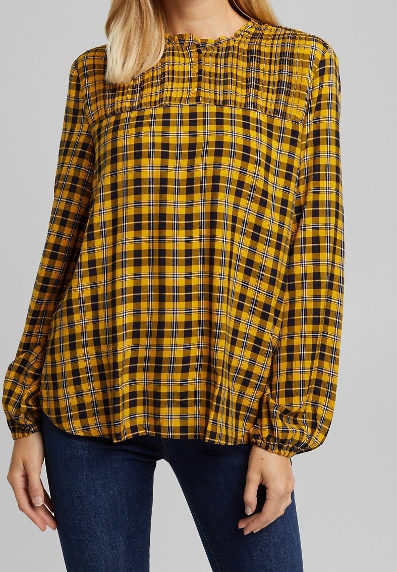 Blusa a quadri giallo e nera con maniche lunghe, scollatura arricciata e dettagli con bottoni, realizzata in tessuto leggero con una consistenza morbida.