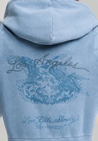 Light blue hoodie with rhinestone-studded "Los Angeles" text, two eagles, skulls, pistols, and "Love Kills Slowly Ed Hardy" design on the back.