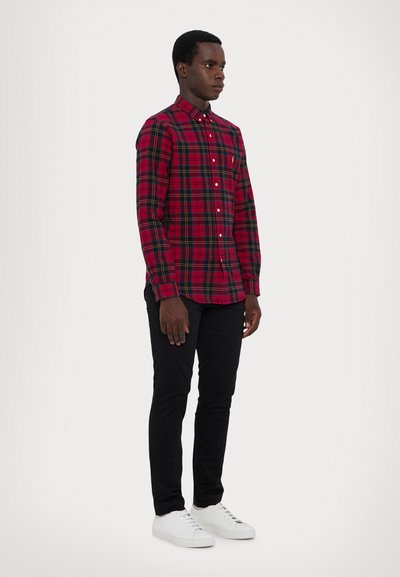 Κόκκινο και πράσινο καρό πουκάμισο με μακρύ μανίκι και κουμπωτή κολάρο, σε συνδυασμό με μαύρο στενό παντελόνι και λευκά αθλητικά παπούτσια. Το πουκάμισο διαθέτει τσέπη στο στήθος.