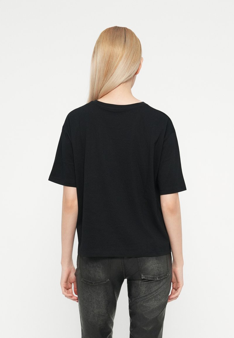 Camiseta de algodón negra de corte relajado, con mangas cortas y cuello redondo. Llevada con jeans oscuros y texturizados. Tejido suave.