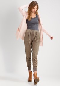 Lys rosa cardigan over en grå tanktop, sammen med olivenfargede, smalere bukser. Brune ankelstøvler med en chunky hæl fullfører looket.