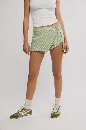 Person iført grønn- og hvit rutete omslagsshorts, hvit ermeløs topp, hvite sokker og grønne joggesko, stående mot en ensfarget bakgrunn.