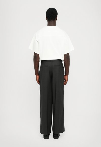 T-shirt bianco a maniche corte abbinato a pantaloni neri larghi, con una texture elegante e una finitura liscia e sartoriale.