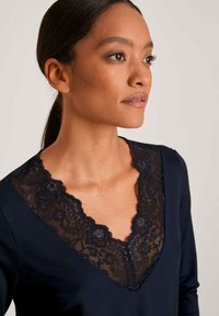 Navy top met een V-hals en delicate zwarte kantdetails langs de halslijn, lange mouwen en een zachte stoftextuur.