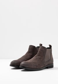 Dark brown suede ankle boots with elastic side panels, rounded toes, and low heels. Features a smooth texture and minimalistic design.