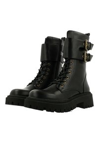Botas de combate de cuero negro con suelas de goma gruesas, cordones en la parte delantera y cremallera lateral; cuentan con dos hebillas decorativas en la parte superior del eje.