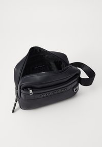 Borsa in pelle nera a forma triangolare, con una cerniera argento, accessori marchiati e un rivestimento interno con motivo che mostra "Armani Exchange."