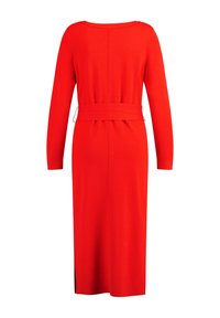 Robe tricotée rouge à manches longues, avec une ceinture à la taille et une longueur mi-mollet. Présente une fente au dos pour faciliter les mouvements et une texture lisse.