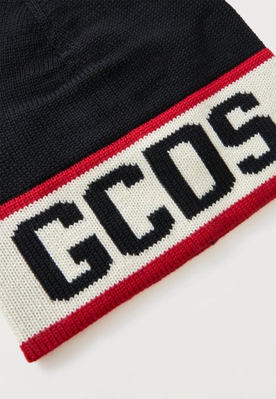 Gros plan d'un bonnet en tricot noir avec une bande rouge et blanche présentant les lettres noires G, C et S.