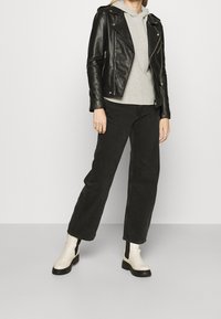 Schwarze Lederbikerjacke über einem grauen Kapuzenpullover, kombiniert mit schwarzen geraden Jeans und cremefarbigen Ankle Boots mit schwarzen Sohlen und elastischen Einsätzen.