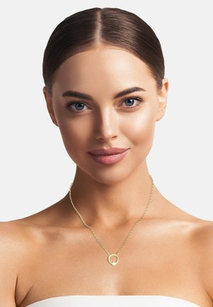 Eine goldene Kettenkette mit einem runden Anhänger und einem kleinen zentralen Edelstein. Glatte Textur und minimalistisches Design.