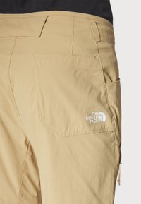 Bežiniai cargo kelnės su užpakaliniu kišenėle, balta The North Face logotipu ir šonine kišenę su užtrauktuku. Minkšta, lengva medžiaga.