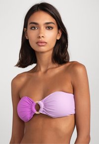 Paarse bandeau bikini top met een geknoopt middenstuk en een ronde accent, gemaakt van gladde stof met een licht glanzende textuur.