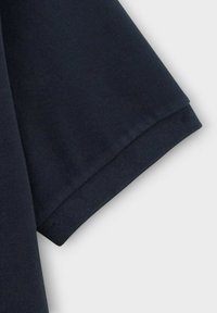 Navyblauwe stof, close-up van een opgevouwen mouw met een gladde textuur en nette stiksels aan de zoom. Eenvoudig ontwerp, geen zichtbare patronen.