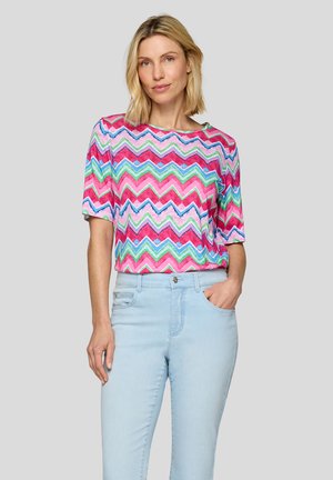 T-Shirt mit kurzen Ärmeln und einem Zickzackmuster in Rosa, Blau und Grün. Lockere Passform mit gerippter Textur, kombiniert mit hellblauen Jeans.