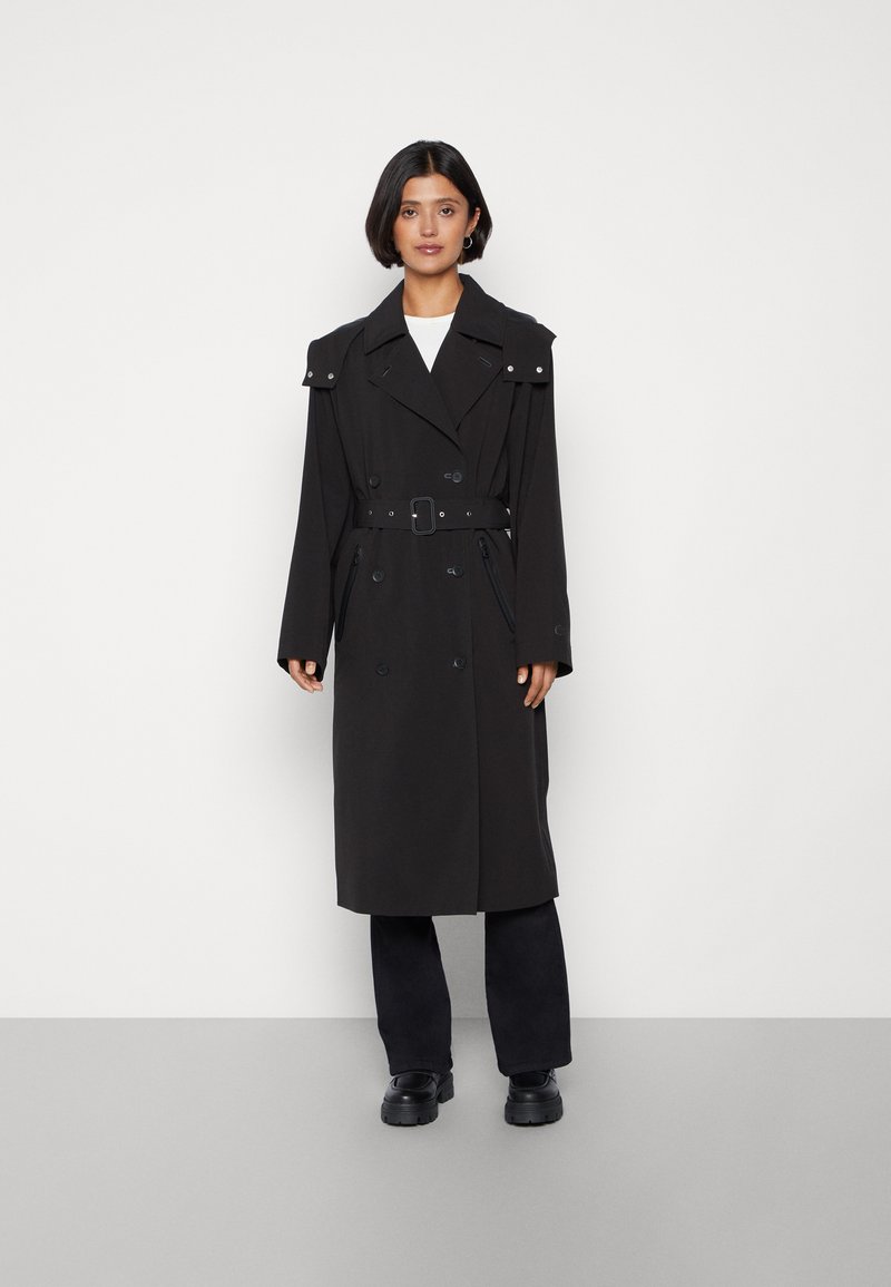 Cappotto nero realizzato in tessuto liscio, caratterizzato da bottoni doppi, vita con cintura, ampio colletto e spalline.