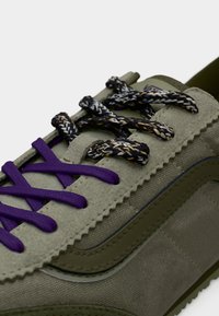 Baskets vert olive avec des lacets à motif mêlant violet et noir, tissu texturé et un design latéral cousu.