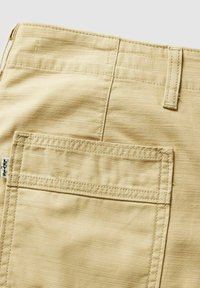 Poche de pantalon beige avec couture visible, passants de ceinture, et petite étiquette en tissu Levi's sur le côté gauche.