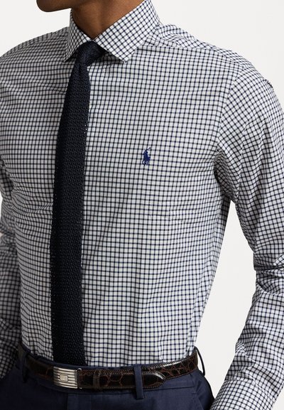 Camisa de botones de cuadros con patrón en azul marino y blanco. Presenta un logo azul, una corbata texturizada en azul marino y un cinturón de cuero oscuro.