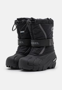 Botas de nieve aislantes en negro con parte superior de textil acolchado, puntera y suela de goma, cuello con cordón ajustable y una marca prominente en las correas.