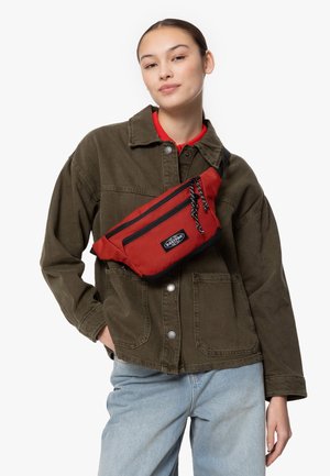 Rote und schwarze Bauchtasche aus strukturiertem Material mit kontrastierendem schwarzen Reißverschluss. Quer über den Körper getragen, mit einem gewebten Gurt und einem Logodetail.
