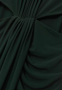 Tume roheline, kerge kangas, millel on peene pleedi ja pehme tekstuur. Materjal langeb sujuvalt, luues voolava silueti.