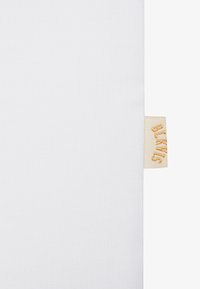 Tissu blanc avec une texture côtelée et une étiquette de marque jaune sur le bord, comportant "SMKS" embossé dans une police stylisée.