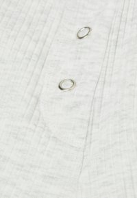 Witte geribde stoffen shirt met drie zilveren metalen knopen en een afgeronde zakomtrek. Zachte textuur met een subtiel patroon.