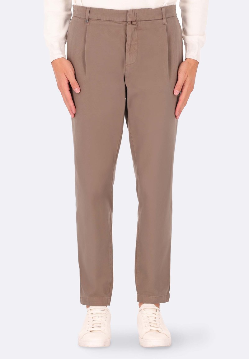 Pantaloni beige a gamba dritta, con pieghe frontali, tasche laterali e passanti per cintura, abbinati a sneakers bianche. Tessuto dalla superficie liscia.