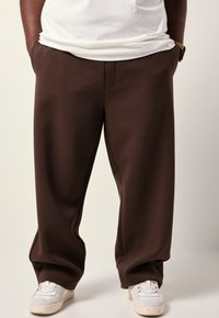 Bruine wijde sweatpants hebben een zachte stof, een elastische tailleband en zijzakken, gecombineerd met witte lage sneakers.