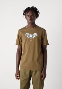 Olive green cotton t-shirt featuring a large bat graphic in black and gray, branded with "BOSS" centered beneath the design.
